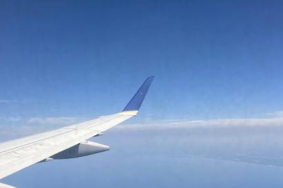 looking out a window of an airplane; one can see part of the airplane's wing and the blue sky