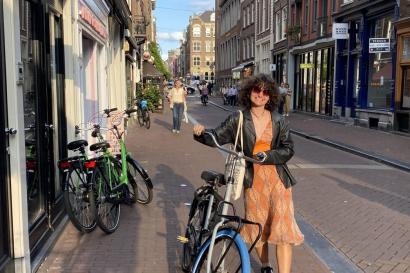 A picture of a student walking with her bicycle down the streets of Amsterdam