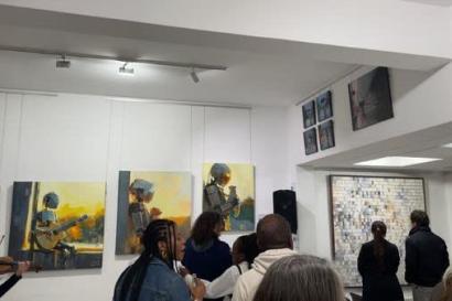 A picture taken at an art gallery featuring multiple pieces of art work and a busy atmosphere. 