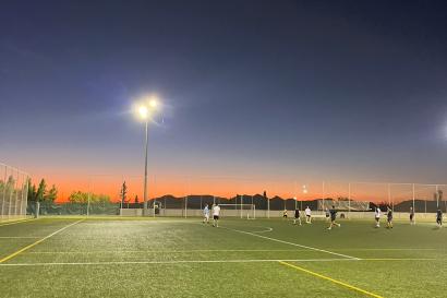The final light from the sunset glows behind the green soccer field, full of players in the middle of a game.