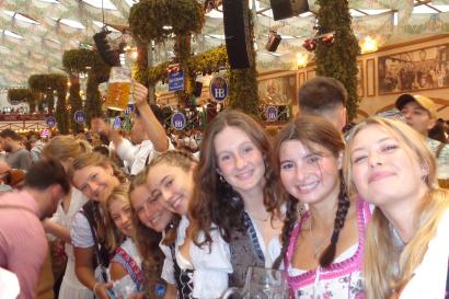 Seven study abroad students dressed in dirndls stand sideways, sandwiched together in the packed room, smiling for the picture in a tent at Oktoberfest.