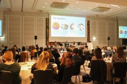 An auditorium with people seated at round tables and panel of people on stage