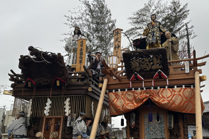 Two of the floats from the Sawara Festival, with members sitting at the top of the float as well as in it. Pictured at the front are the people who help pull the float.