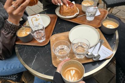 A table filled with pastries and coffee, a group of friends socializing. 