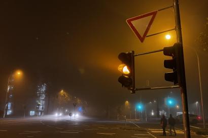 A foggy street with traffic lights and some cars