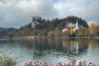 A large lake with a castle seen in the background on a large cliff with a small church at the foreground. 