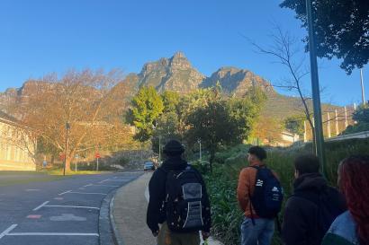 Image of three students walking to school with backpacks on with the iconic devils peak and table mountain in the background. 