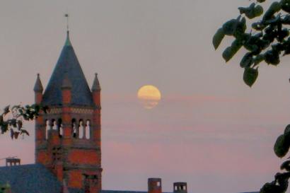 An image of a beautiful sunset, a bright moon, and a historical building.