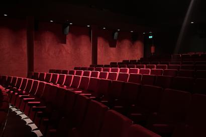 Dimly lit movie theater with red velvet seating and red curtains adorning the walls. 