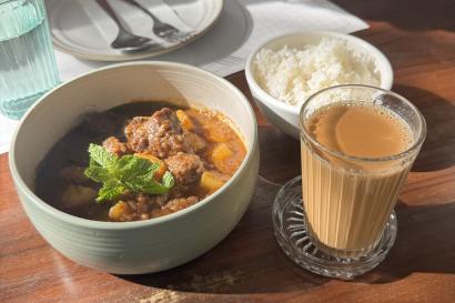 a meal consisting of a bowl of curry, a bowl of rice, and some milk tea