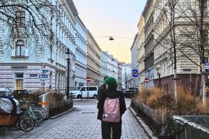 Two friends are walking the streets of Vienna, on a street centered between tall buildings encapsulating the scenery on the left and right.