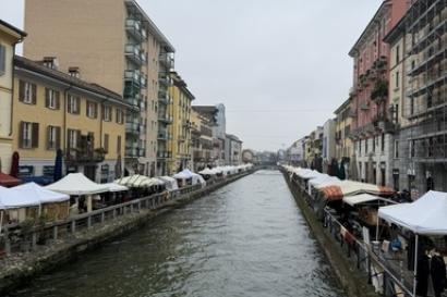 The photo shows a stretch of canal with tall buildings on either side. Two rows of white tents go out into the horizon. 