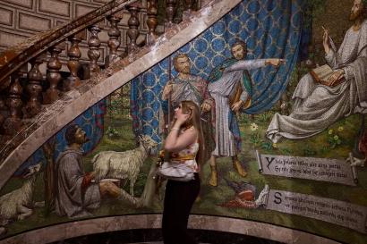 A curved staircase depicts a scene of men lining up under a bright blue sky. A woman stands in the center, looking up in thoughtful contemplation. 