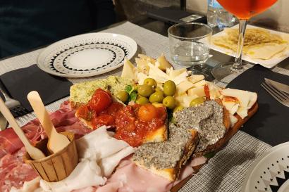 A table filled with Italian aperitivo dishes including cured meats, cheeses, olives, bruschetta, and bread, served with an Aperol Spritz at a restaurant in Milan.