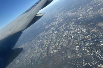 View outside of a plane window showing the Chicago metropolitan area, the right wing of a plane, and a blue sky.