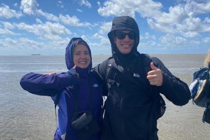 Two students smile and thumbs up for the camera, standing in the ocean
