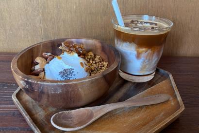 A latte and a yogurt bowl with granola and honey served on a six-sided wooden tray with a wooden spoon.