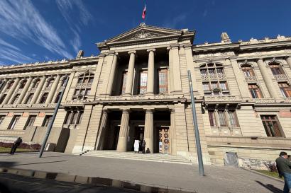 A large, tan building with pillars and detailed architecture with a Chilean flag stands against a blue sky filled with clouds. 
