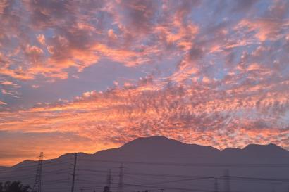 Vibrant oranges spread across the horizon and puffy clouds scatter the sky, the dark silhouette of the Andes mountains is a stark contrast to the colors.