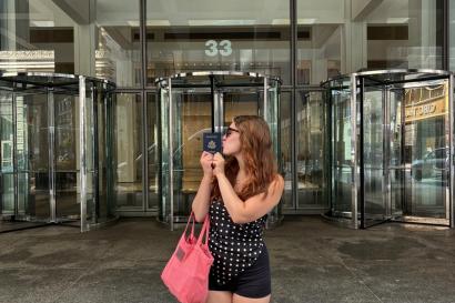 The author stands in profile, kissing the side of a passport in front of a building lobby
