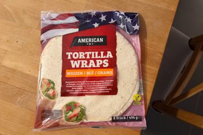 A bag of tortilla wraps labeled "American" rests on a wooden table.