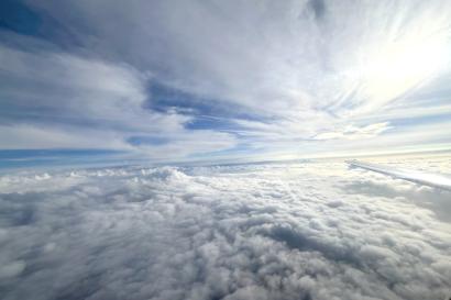 A wide shot of a blue sky covered in white clouds from the window of an airplane.