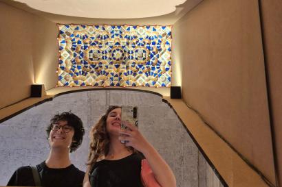 Two students take a mirror selfie with a mocarabe design above them.