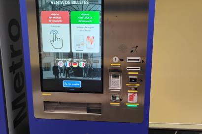 This is a blue Metro ticket machine with a large touch screen in the center. Above the screen, from left to right: Card slot for bank cards, Cash note slot, Contactless card area, Ticket/card slot with a green light, Keypad with a small display, Ticket/receipt output slot. On the screen you can choose ticket options and languages, and there is an accessible-use button with a wheelchair symbol. Summary provided by Be My Eyes AI.