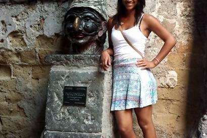 Crowd gathered on a busy street.

Standing woman in a green dress with arms outstretched in front of historic building.

Woman in a skirt next to a stone sculpture with a plaque on a narrow street. This alt text was added with Al; accuracy may vary.