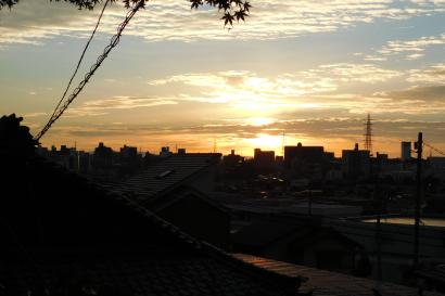 Sunset over a city skyline with silhouetted rooftops and clouds. This alt text was added with Al; accuracy may vary.