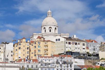 Large domed building in Lisbon with colorful houses, under a blue sky. This alt text was added with Al; accuracy may vary.
