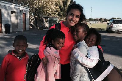 Smiling woman and four children hugging outdoors, sunny day. This alt text was added with Al; accuracy may vary.