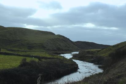 River winding through green hills under a cloudy sky. This alt text was added with Al; accuracy may vary.