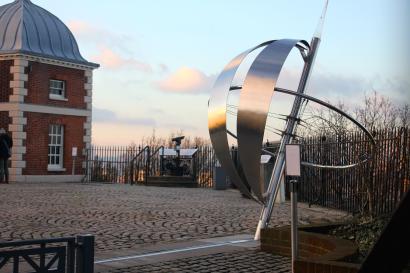 Prime Meridian sculpture at Greenwich Observatory, sunset sky in background. This alt text was added with Al; accuracy may vary.