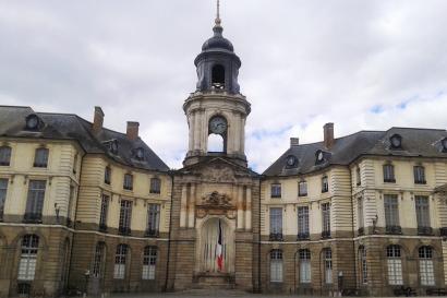Elegant building with a central clock tower under a cloudy sky. This alt text was added with Al; accuracy may vary.