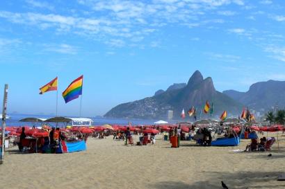 Crowded Rio de Janeiro beach with colorful flags and umbrellas under a blue sky. This alt text was added with Al; accuracy may vary.