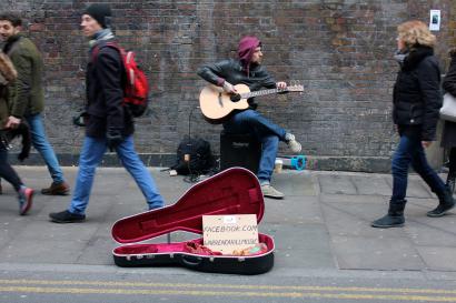 Street guitarist playing with open case on busy sidewalk. This alt text was added with Al; accuracy may vary.