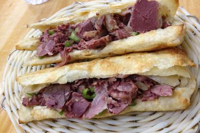 Two stacked flatbread sandwiches with sliced meat and herbs. This alt text was added with Al; accuracy may vary.