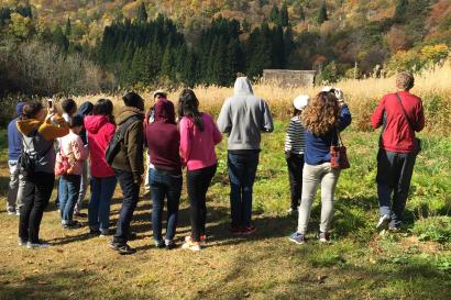 Group of people gathered in a field with mountains in the background, under a clear blue sky. This alt text was added with Al; accuracy may vary.
