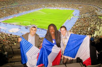 Three people holding French flags at a crowded stadium. This alt text was added with Al; accuracy may vary.