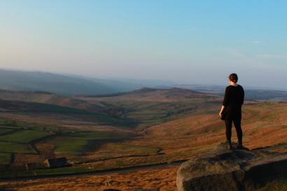 Standing on a hill, person gazes over vast, rolling landscape at sunset. This alt text was added with Al; accuracy may vary.
