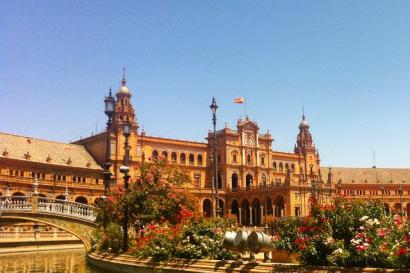 1. Tall stone church tower under cloudy sky.
2. Interior with blue stained glass and Christ figure.
3. Group of people posing before ornate archway.
4. Plaza with grand building and water canal. This alt text was added with Al; accuracy may vary.