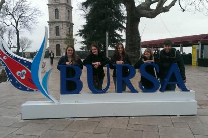 1. Cityscape with distant hills under a blue sky.
2. Colorful tulip garden near a reflective pond.
3. Messy room with cluttered items on a bed.
4. Rainbow over a lake with a castle and trees.
5. Group posing behind a "Bursa" sign in a plaza. This alt text was added with Al; accuracy may vary.