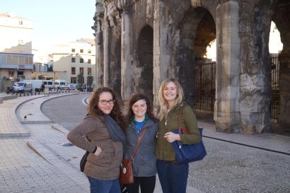 Three people smiling in front of ancient stone arches on a sunny day. This alt text was added with Al; accuracy may vary.
