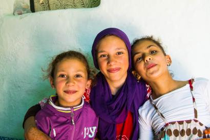 A diverse group of friends smiling by a riverside, with historic buildings in the background. This alt text was added with Al; accuracy may vary.