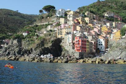 Colorful hillside village by the sea, with cliffs and a small boat. This alt text was added with Al; accuracy may vary.