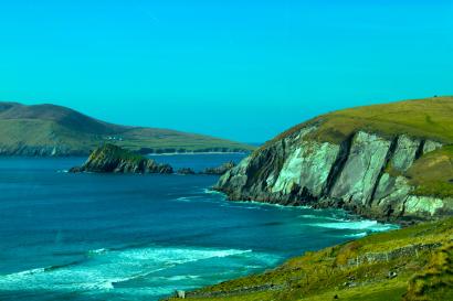 Rocky coastline with cliffs beside a vibrant blue sea and clear sky. This alt text was added with Al; accuracy may vary.