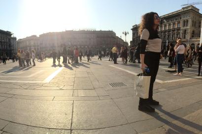 Historic square with people walking and buildings in the background under bright sunlight. This alt text was added with Al; accuracy may vary.