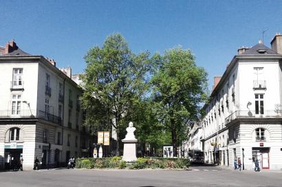 Spacious city square with people walking, sunlit buildings, and a clear sky. This alt text was added with Al; accuracy may vary.