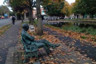 Night view of Sagrada Familia with illuminated spires and cranes. 

Park bench statue, surrounded by autumn leaves, with trees lining a path. This alt text was added with Al; accuracy may vary.